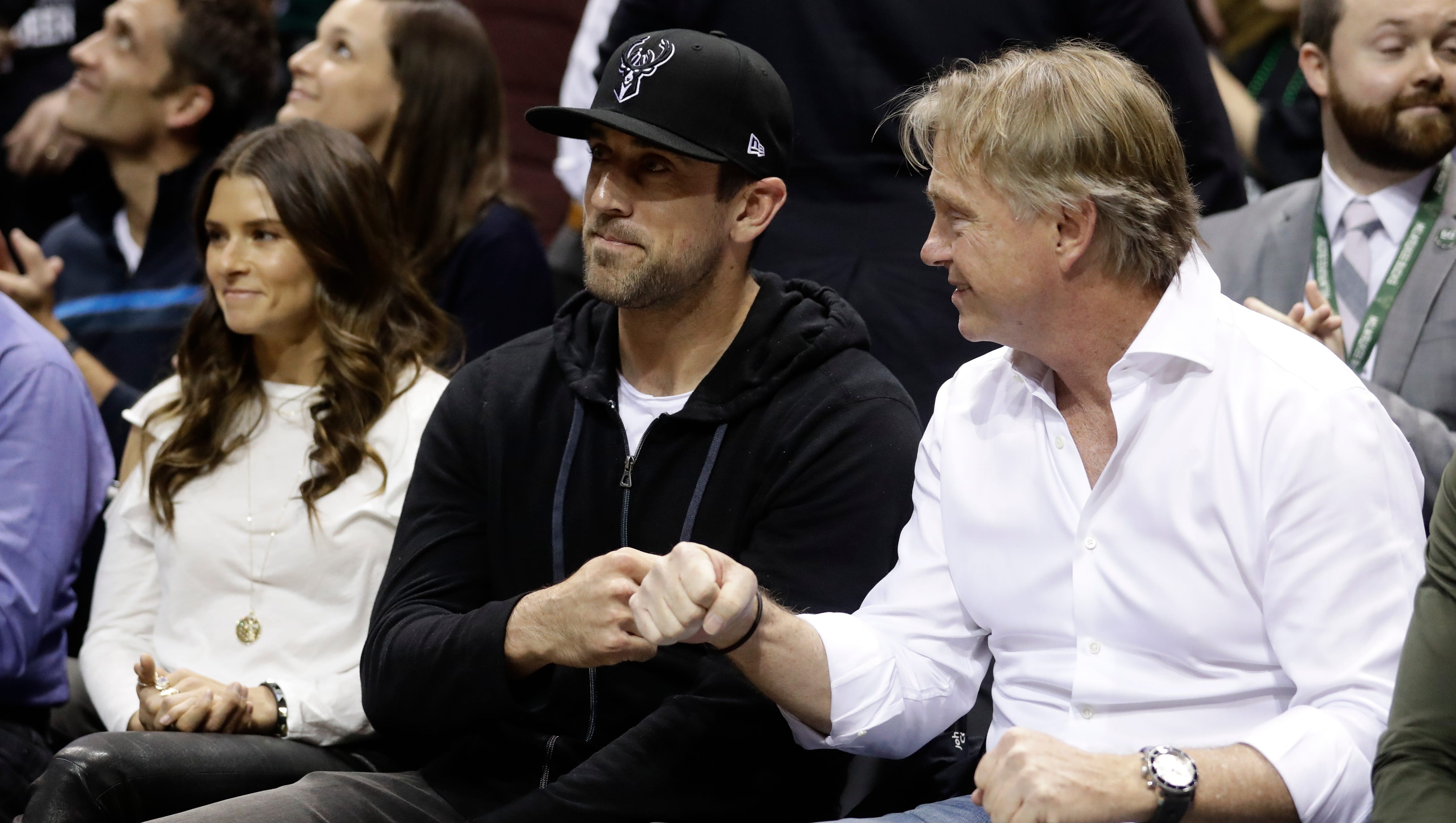 Aaron Rodgers and Wes Edens do a fist bump during Game 3 of the Bucks-Celtics playoff game, where it was announced that Rodgers had joined the Bucks' ownership group. Race car driver, Danica Patrick, looks on during the game.