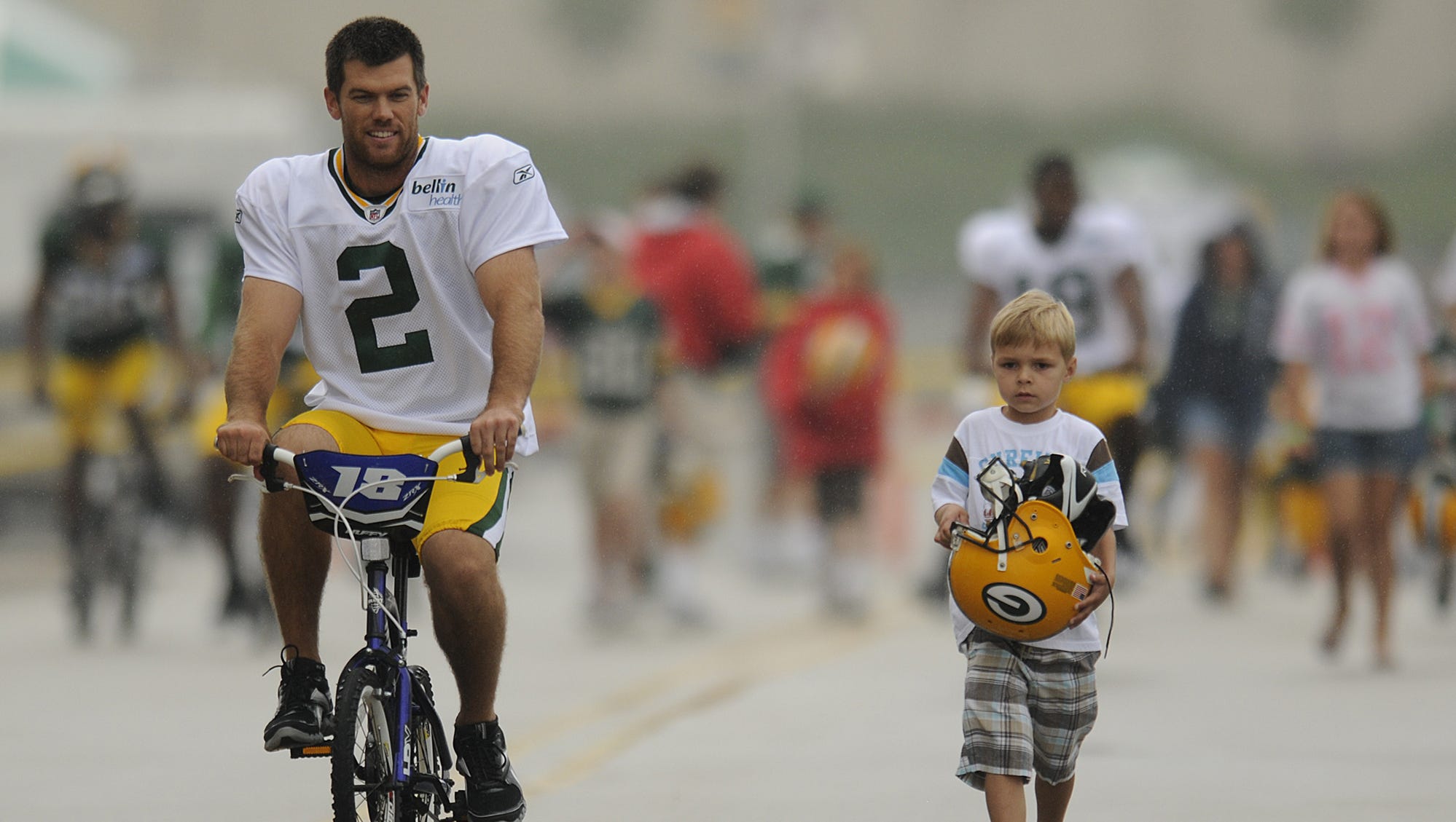 At right, Mason Chaltry, 5, of Howard, lets Green Bay Packers kicker Mason Crosby (2) ride his bike as he carries Crosby's helmet to training camp practice on July 31, 2010, at Ray Nitschke Field.