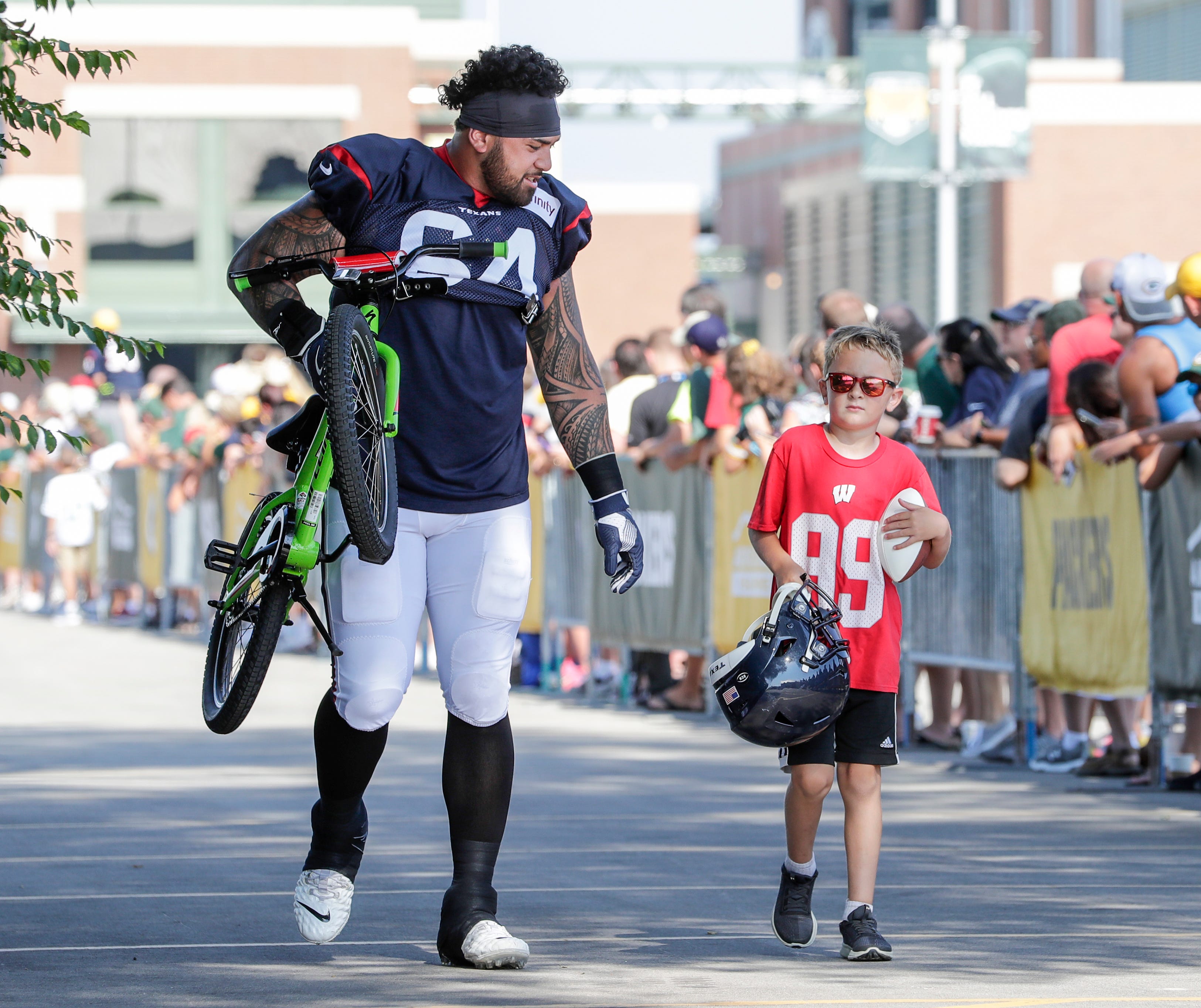 Texans guard Senio Kelemete (64) carries a bike to Clarke Hinkle Field for a joint training camp practice with the Green Bay Packers Monday, August 5, 2019, in Ashwaubenon, Wis.